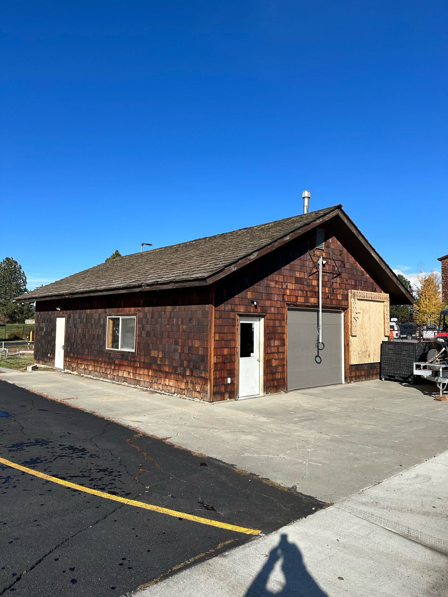 Before photo of McCall Smoke Jumper Base outbuilding — weathered cedar shake siding with aging roof and garage door