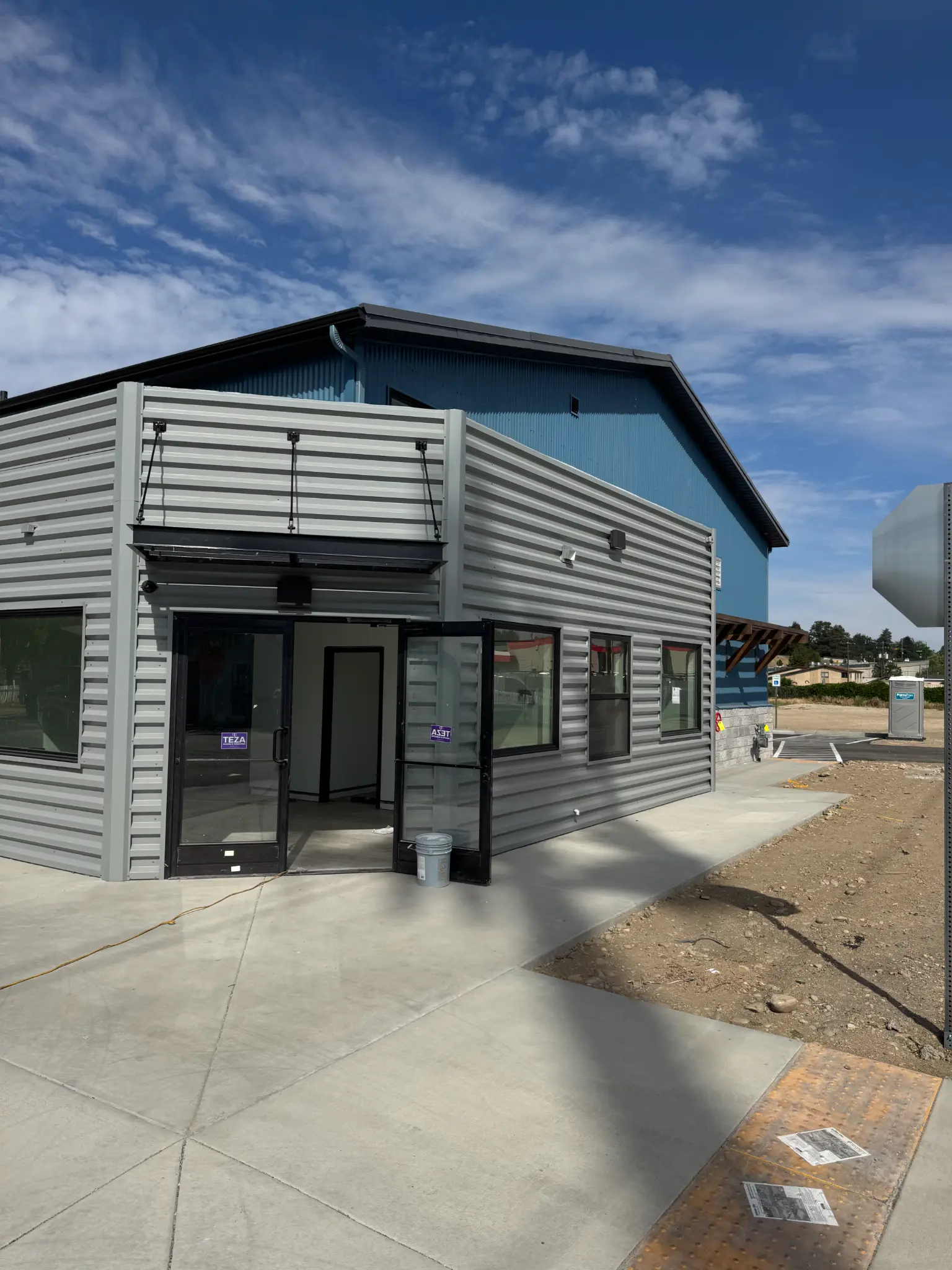 After photo of commercial building front corner with finished gray corrugated steel siding, glass storefront entry doors, and canopy above entry