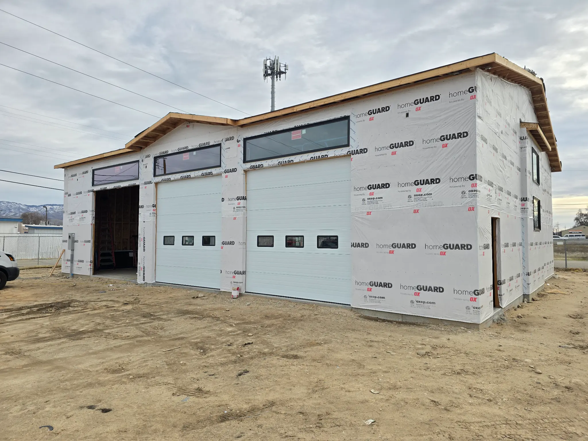 Before photo of commercial building warehouse front showing two roll-up garage doors and clerestory windows wrapped in HomeGuard housewrap