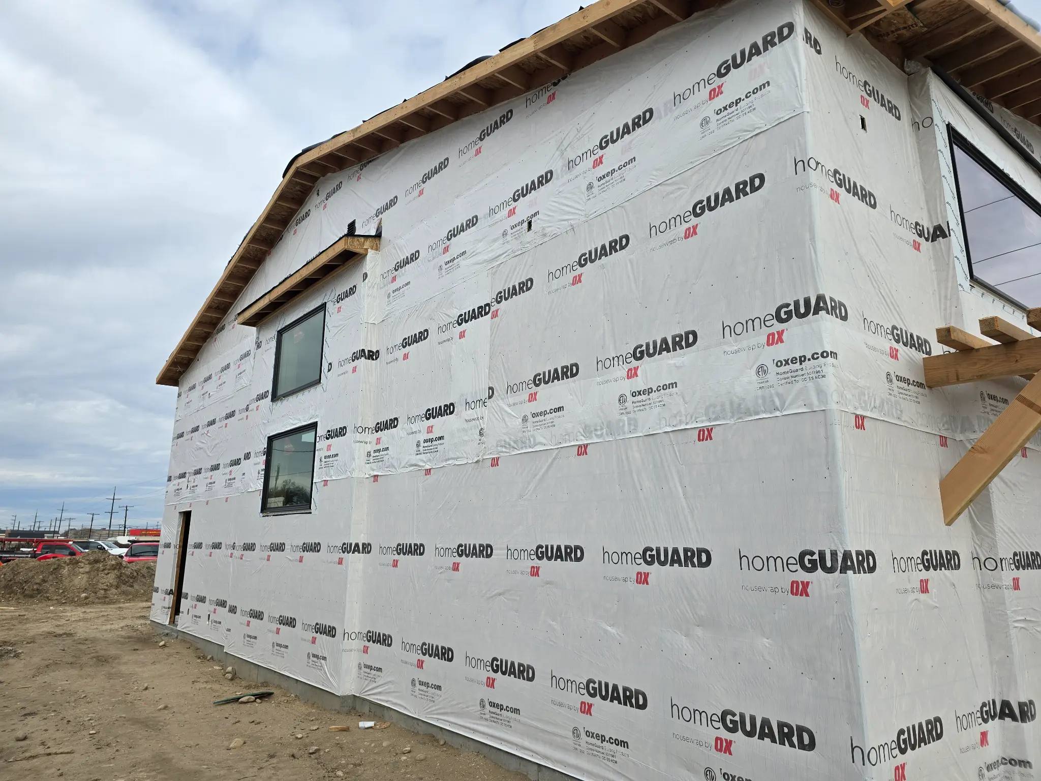Before photo of commercial building warehouse side wall wrapped in HomeGuard housewrap, showing two stacked windows and the corner transition to the office wing